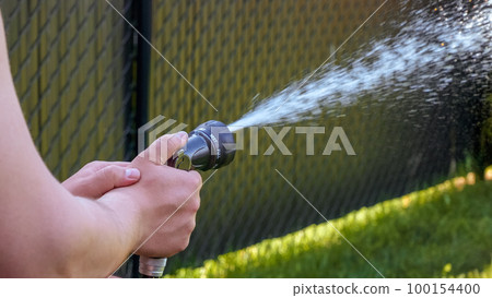 Hose watering plants in the garden by the farmer. Watering with gun nozzle. Shallow depth of field 100154400