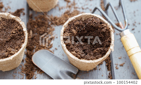Close up of hand in yellow glove planting a seed in eco friendly biodegradable peat pots, top view, selective focus. Spring natural gardening, eco, plant care, organic product 100154402