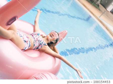 Asian young woman relax on pink flamingo inflatable looking up at pool villa Asian young woman relax on pink flamingo inflatable looking up at pool villa 100154453