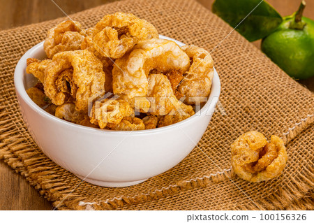 High angle view of homemade crispy deep fried pork rinds in white ceramic bowl on sack cloth. High angle view of homemade crispy deep fried pork rinds in white ceramic bowl on sack cloth. 100156326