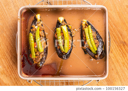 Top view of hot delicious turkey stuffed eggplants - karniyarik in golden tray metal ovenware on metal cooling rack on wooden table. Top view of hot delicious turkey stuffed eggplants - karniyarik in golden tray metal ovenware on metal cooling rack on wooden table. 100156327