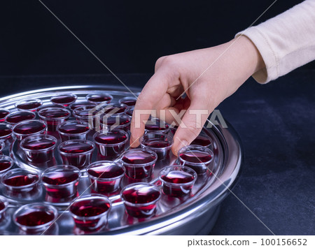 Closeup of young woman taking communion from small cups on black background 100156652