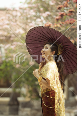 asian woman holding bamboo umbrella standing against plumeria flower blooming in old temple ayutthaya thailand 100160687