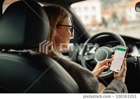 Female driver in glasses using phone with gps navigation app on screen while traveling by car 100163201
