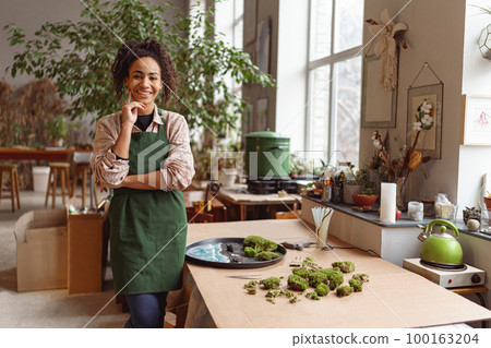 Portrait of woman decorator in process of making green ikebana in florist workshop looking at camera 100163204