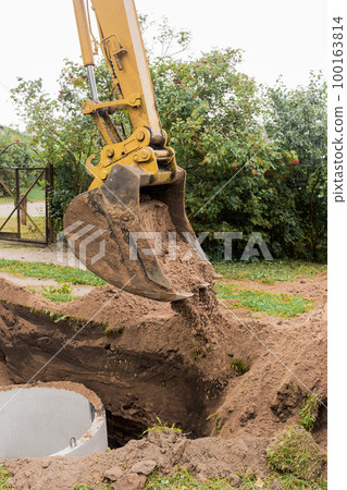 A bucket of excavator with a pile of sand and earth buries sewer concrete rings in the industrial zone A bucket of excavator with a pile of sand and earth buries sewer concrete rings in the industrial zone 100163814