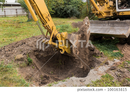 A bucket of excavator pours the ground into a heap against the background of a rural industrial zone. Bulldozer work on the construction site A bucket of excavator pours the ground into a heap against the background of a rural industrial zone. Bulldozer work on the construction site 100163815