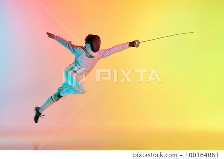 Long attack. Young man, male fencer with sword practicing in fencing over gradient pink-yellow background in neon light. Sportsman shows fencing technique 100164061