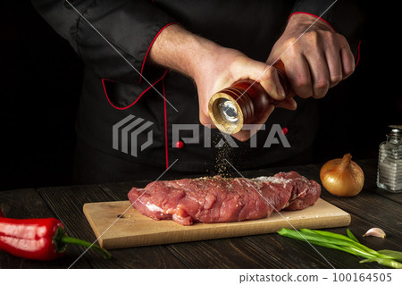 The chef prepares the veal meat and adds pepper or chili. Working environment in the kitchen during barbecue. Asian cuisine The chef prepares the veal meat and adds pepper or chili. Working environment in the kitchen during barbecue. Asian cuisine 100164505