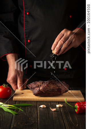 The chef sprinkles the baked beef meat with salt. Work environment on the kitchen table. Asian cuisine. The chef sprinkles the baked beef meat with salt. Work environment on the kitchen table. Asian cuisine. 100164508
