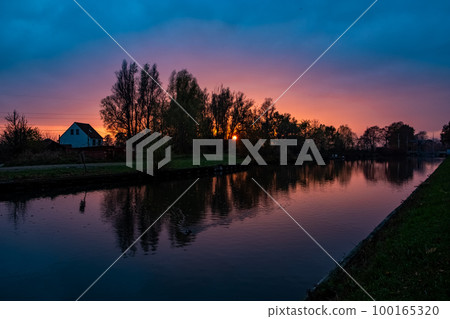 Beautiful sunset over a river with green bushes and color rich sky Beautiful sunset over a river with green bushes and color rich sky 100165320