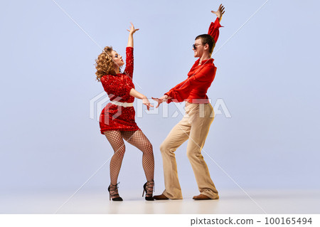 Young beautiful couple of dancers in bright retro fashion clothes, stage costumes dancing over lilac color background. Concept of music, art, dance, retro Young beautiful couple of dancers in bright retro fashion clothes, stage costumes dancing over lilac color background. Concept of music, art, dance, retro 100165494