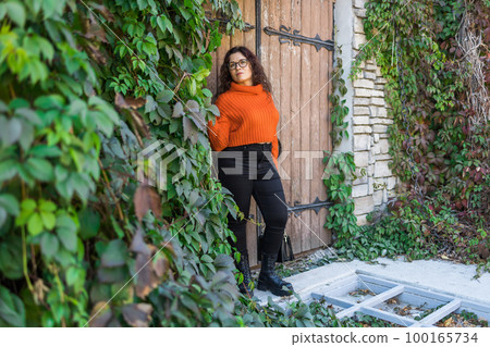 Portrait of carefree young woman smiling with big door background. Cheerful latin girl wearing eyeglasses in the city. Happy brunette woman with curly hair and spectacles smiling. Copy space and empty Portrait of carefree young woman smiling with big door background. Cheerful latin girl wearing eyeglasses in the city. Happy brunette woman with curly hair and spectacles smiling. Copy space and empty 100165734