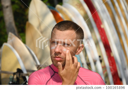 Man surfer applies protective zinc on his face. Preparing to surf. UV protection. Man surfer applies protective zinc on his face. Preparing to surf. UV protection. 100165896
