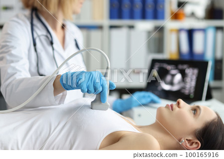 Doctor holds ultrasound probe on chest of patient in clinic closeup 100165916