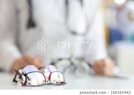 Ophthalmologist sits in background with various glasses for fitting lenses in frame Ophthalmologist sits in background with various glasses for fitting lenses in frame 100165942