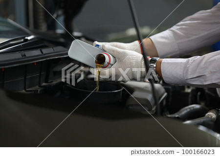 Auto mechanic pours oil into car engine from cans of oil 100166023