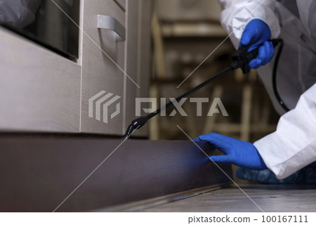 An exterminator in work clothes sprays pesticides with a spray gun. Fight against insects in apartments and houses. Disinsection of the premises 100167111