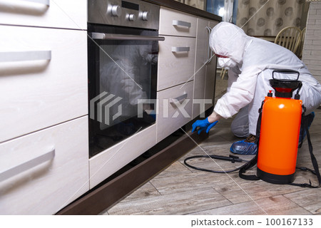 An exterminator in work clothes sprays pesticides with a spray gun. Fight against insects in apartments and houses. Disinsection of the premises 100167133