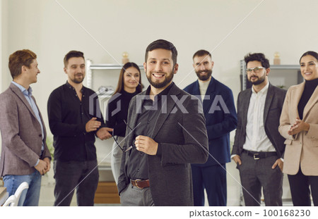 Happy employees applaud an excited, handsome brunette man in black suit, greet new team member at work. Happy employees applaud an excited, handsome brunette man in black suit, greet new team member at work. 100168230