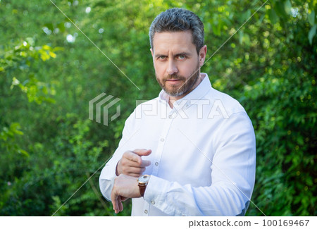 Professional man pointing finger at wristwatch natural background, punctuality 100169467