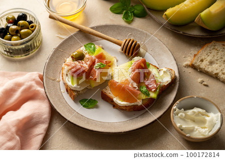 Melon with prosciutto toast with basil and honey. Antipasti snack. 100172814