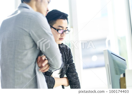 two young asian business people working together in office discussing business using desktop computer two young asian business people working together in office discussing business using desktop computer 100174403