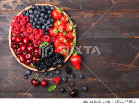 Fresh organic summer berries mix in round wooden tray on dark wooden table background. 100174608