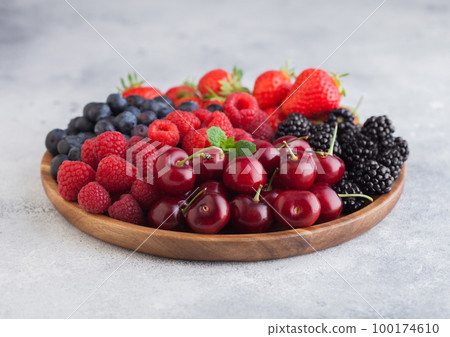 Fresh organic summer berries mix in round wooden tray on light kitchen table background 100174610