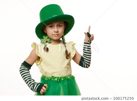 Adorable Caucasian little girl dressed as Leprechaun in green hat and striped gloves with clover leaves, for St. Patrick's Day party, points her index finger at copy space for ads on white background Adorable Caucasian little girl dressed as Leprechaun in green hat and striped gloves with clover leaves, for St. Patrick's Day party, points her index finger at copy space for ads on white background 100175250