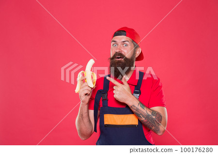 Hungry hipster. Favorite snack. Food court. Lunch time. Bearded man in uniform and cap eating banana. Worker builder mechanic eat banana. Fresh fruit. Living healthy life. Tasty food. Bite banana Hungry hipster. Favorite snack. Food court. Lunch time. Bearded man in uniform and cap eating banana. Worker builder mechanic eat banana. Fresh fruit. Living healthy life. Tasty food. Bite banana 100176280