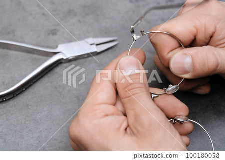 Closeup of optician's hands repairing broken eyeglasses frame using special pliers in clinic office 100180058