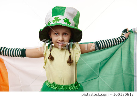 Adorable Caucasian little child girl dressed as Leprechaun in hat with clover leaves and striped gloves, smiling looking at camera, carrying Ireland flag, white background. Saint Patrick's day concept Adorable Caucasian little child girl dressed as Leprechaun in hat with clover leaves and striped gloves, smiling looking at camera, carrying Ireland flag, white background. Saint Patrick's day concept 100180612