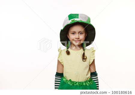 Adorable Irish little child girl wearing clover leaves earrings and green hat, smiles looking at camera, standing isolated over white background. Traditions, culture and national holiday in Ireland 100180616