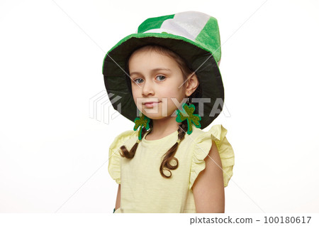 Studio shot of stylish Irish little baby girl dressed like a Leprechaun for St Patrick's Day party, wearing clover leaves earrings and green hat, smiles looking at camera, isolated on white background Studio shot of stylish Irish little baby girl dressed like a Leprechaun for St Patrick's Day party, wearing clover leaves earrings and green hat, smiles looking at camera, isolated on white background 100180617