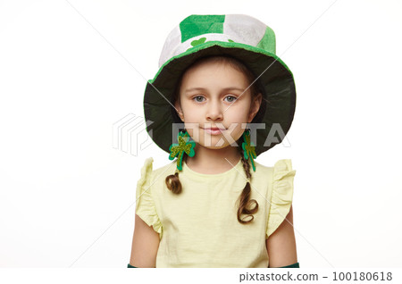 Close-up portrait of a pretty little child girl wearing a Saint Patrick's green hat with clover leaves, confidently looking at camera, isolated on white background. Irish traditions and cultures 100180618