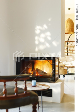 Cup of hot drink on table, warm fireplace with armchair in front and natural light from window Cup of hot drink on table, warm fireplace with armchair in front and natural light from window 100180625