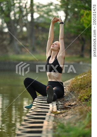 Athletic woman stretching arms after workout session in the park near lake on a sunny summer morning. Healthy lifestyle concept Athletic woman stretching arms after workout session in the park near lake on a sunny summer morning. Healthy lifestyle concept 100181478
