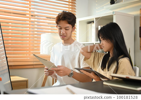 Asian male tutor helping young student with homework at desk in bright room. Homeschooling, education and people concept 100181528