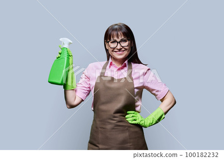 Middle aged woman in gloves apron with organic detergent on grey background 100182232