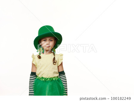 Charming Irish little child girl with two funny pigtails, wearing a Leprechaun carnival costume and clover leaf earrings, looking at camera, isolated over white background. Saint Patrick's Day concept 100182249