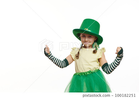 Adorable Irish little girl in Leprechaun carnival costume for St. Patrick's Day, thumbing up looking at camera, isolated on white background. Culture and traditions in Ireland. People and life events 100182251