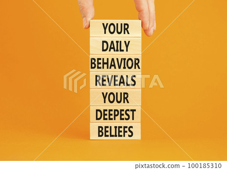Behavior symbol. Concept words Your daily behavior reveals your deepest beliefs on wooden blocks. Beautiful orange background. Copy space. Businessman hand. Motivational business behavior concept. 100185310