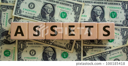 Concept word 'assets' on wooden cubes on a beautiful background from dollar bills. Business concept. Concept word 'assets' on wooden cubes on a beautiful background from dollar bills. Business concept. 100185418