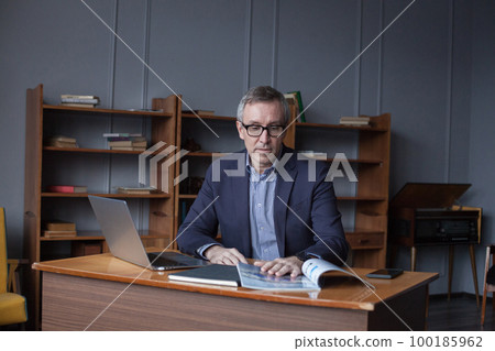 Portrait of mature serious businessman in suit and glasses reading book  in office 100185962