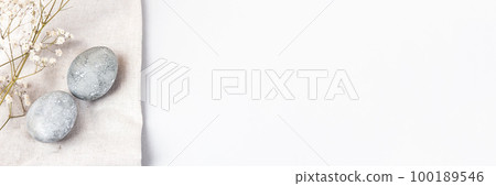 Grey Easter eggs with a sprigs of gypsophila on a linen towel on a grey background. Minimalism, copy space, banner 100189546