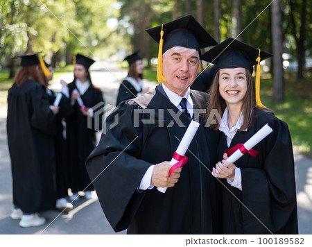 A group of graduates in robes outdoors. An elderly man and a young woman congratulate each other on their graduation. A group of graduates in robes outdoors. An elderly man and a young woman congratulate each other on their graduation. 100189582