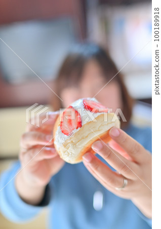 A woman eating a large fruit sandwich filled with whipped cream and strawberries Local gourmet food for a camper trip 100189918
