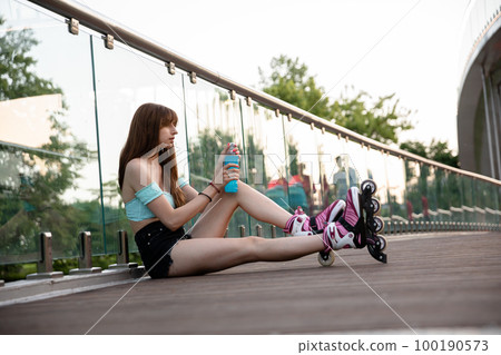 Skater girl sitting on bridge opens drink bottle Skater girl sitting on bridge opens drink bottle 100190573