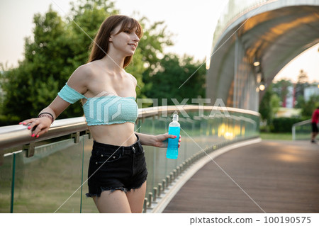 A smiling young woman leans against a metal railing on a bridge. 100190575